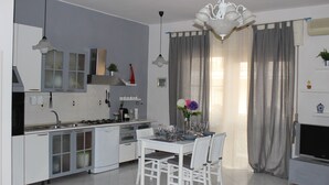 A modern kitchen with white cabinetry, a dining table with chairs, and a chandelier. - Raffy's House Pompeii (Scafati)