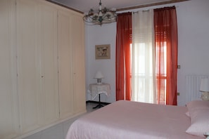 A bedroom with a bed, a nightstand, a lamp, a wardrobe, and a window with curtains.