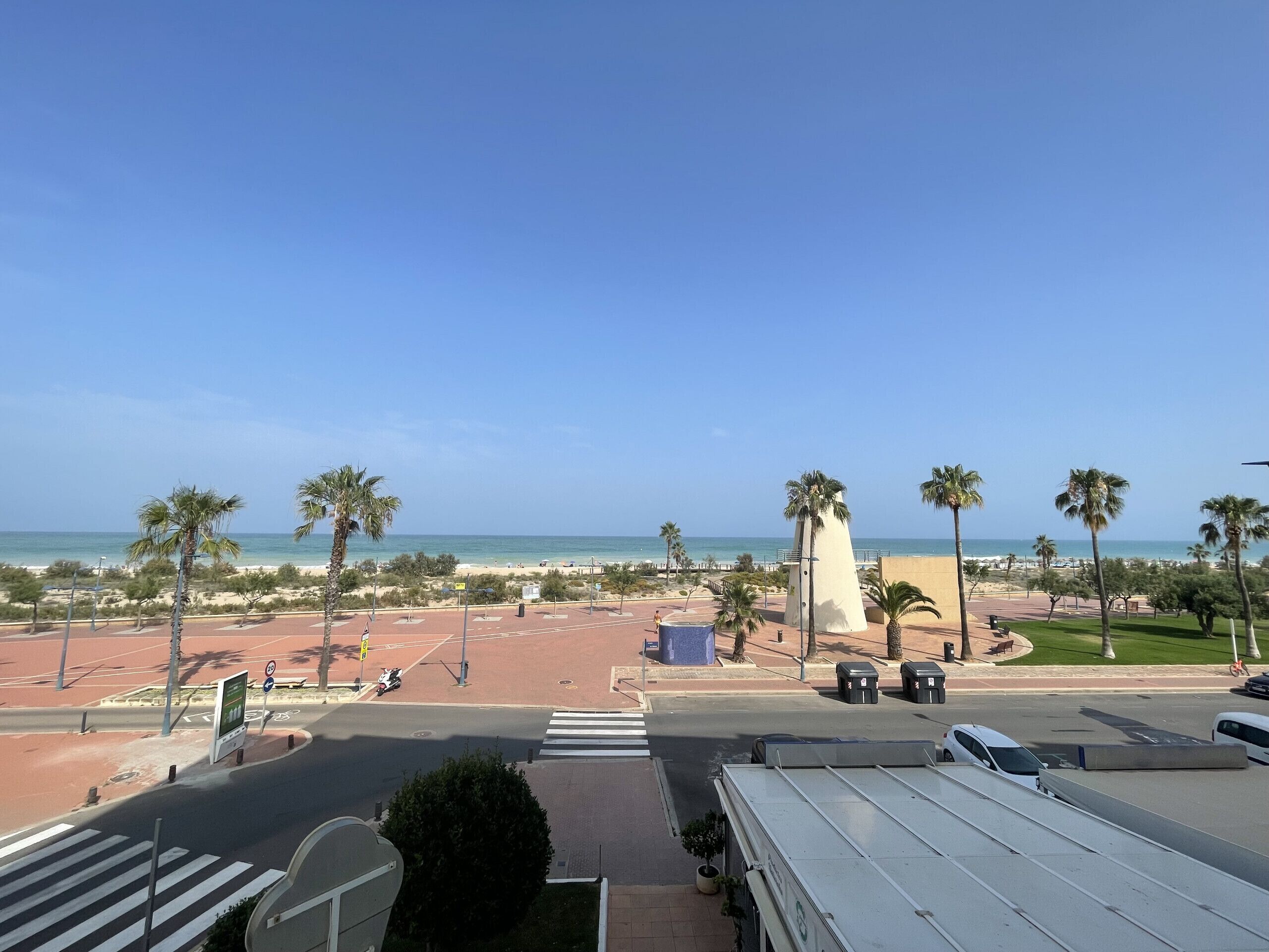 A coastal view with a beach, palm trees, and a clear sky.