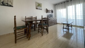 A dining area with a wooden table and chairs, a television on a cabinet, and a large window with sheer curtains. - Peñismar I D 2-10 (Peñiscola)