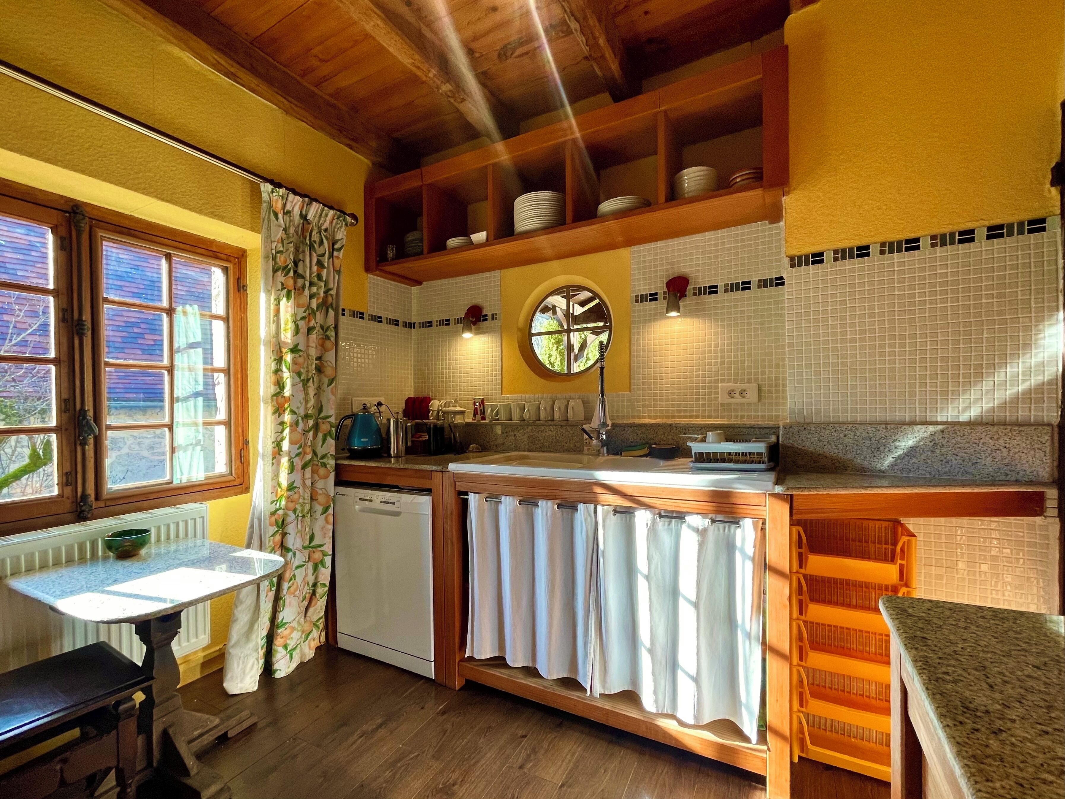 Une cuisine avec des meubles de rangement en bois, un évier, une fenêtre avec des rideaux et une horloge au mur.