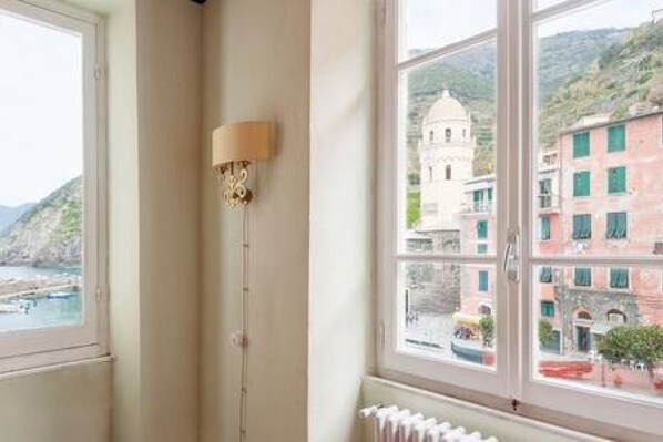 A room with a large window overlooking a coastal town with buildings and hills.