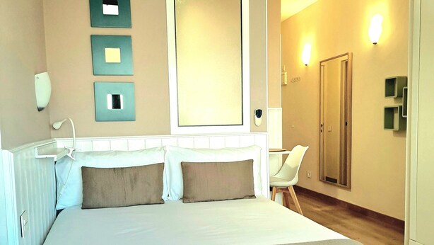 Une chambre d’hôtel avec un grand lit, un miroir, une chaise et une porte.