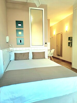 A hotel room with a large bed, a mirror, a chair, and a door.