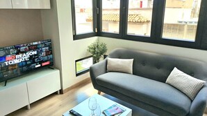 Un salon avec un canapé gris, une table basse blanche sur laquelle se trouvent une télécommande et un verre, et un téléviseur qui affiche une sélection de films.