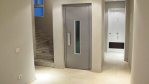Un couloir avec une porte grise, un escalier et, au fond, une porte blanche.