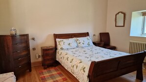 A bedroom with a wooden bed, a dresser, a nightstand, a chair, and a window with a view. - Watergreens Farm, CA9 3LD  Self-Catering holiday Accommodation in Cumbria (Alston)