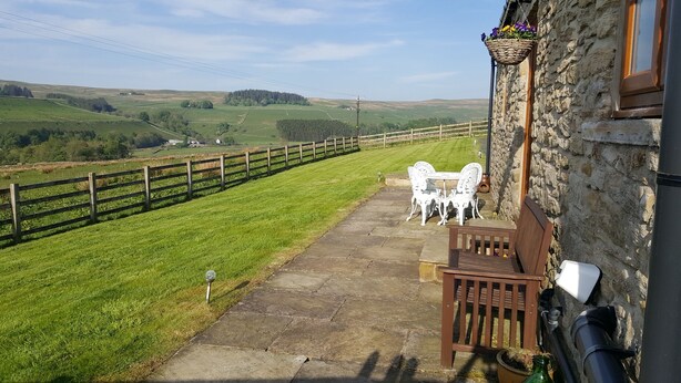A stone building with a patio, white outdoor furniture, and a view of green fields. - Watergreens Farm, CA9 3LD  Self-Catering holiday Accommodation in Cumbria (Alston)