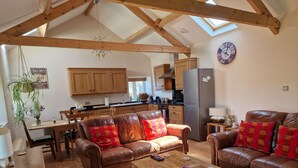 A spacious living room with leather sofas, a wooden coffee table, and a dining area with a wooden table and chairs. A kitchen with wooden cabinets and a refrigerator is visible in the background. - Watergreens Farm, CA9 3LD  Self-Catering holiday Accommodation in Cumbria (Alston)
