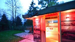 Una cabaña de troncos con fachada de madera, una entrada visible y un pequeño espacio al aire libre con mesa y sillas.