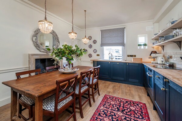 A kitchen with a wooden dining table, chairs, a chandelier, and blue cabinets.