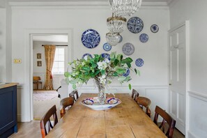A dining room with a wooden table, chairs, a chandelier, and blue and white patterned plates on the wall.