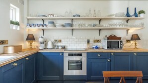 Uma cozinha com armários azul escuro, forno embutido, micro-ondas e uma mesa de madeira.
