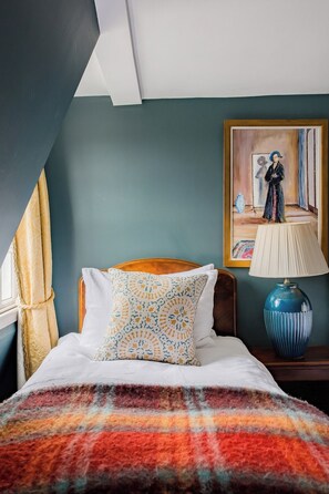 A bedroom with a bed, a painting, a lamp, and a patterned pillow.