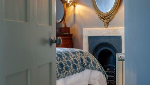 Quarto com cama, lareira, espelho e luminária na parede.
