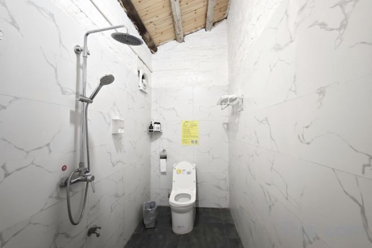 A small, compact bathroom with a shower, toilet, and a trash bin.