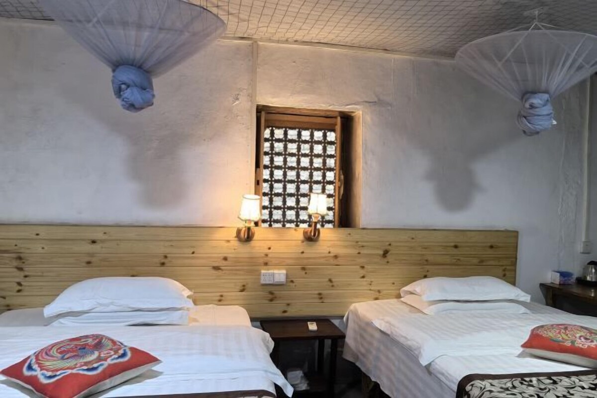 A room with two beds, a wooden headboard, a window with a grid pattern, and wall-mounted lamps.