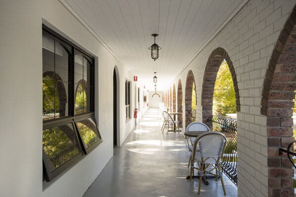 A corridor with arched brick walls, a row of tables and chairs, and a fire extinguisher on the wall.