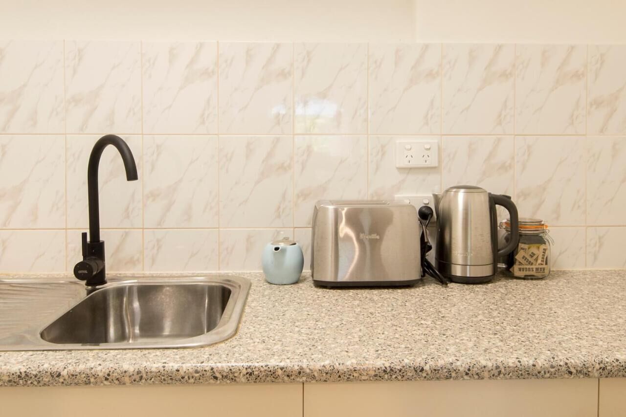 A kitchen with a sink, a toaster, a kettle, and a jar of sugar.