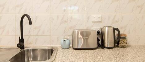 A kitchen with a sink, a toaster, a kettle, and a jar of sugar.
