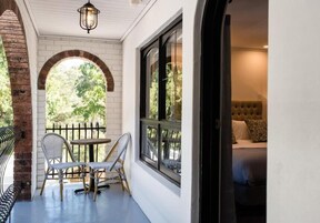 A cozy balcony with wicker furniture, a view of greenery, and a tufted headboard bed inside.