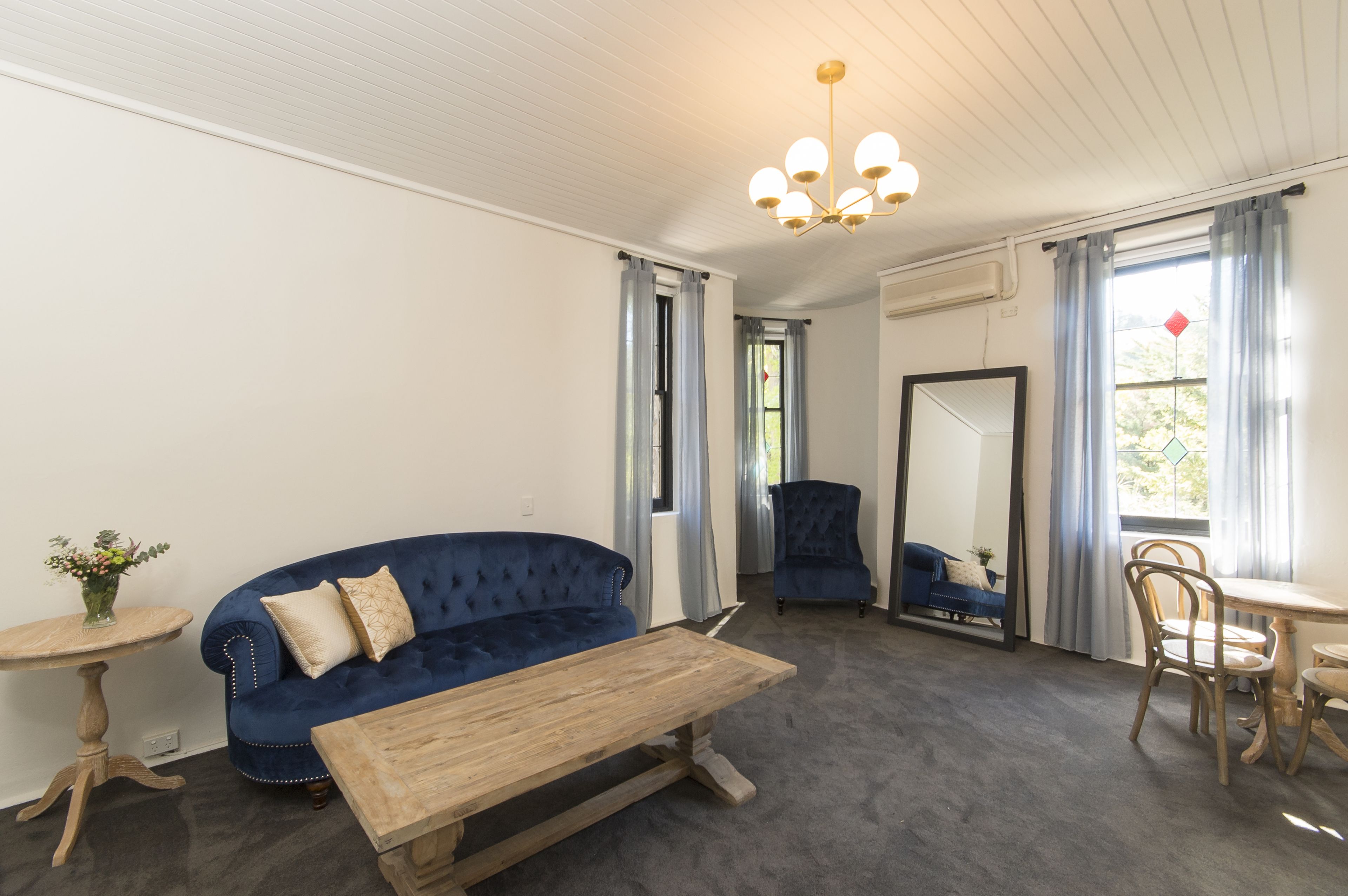 A room with a blue sofa, a wooden table, a mirror, and a chandelier.