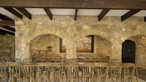 A stone-walled room with a long table and chairs, wooden beams, and a door. - The Manor Basket Range (Basket Range)