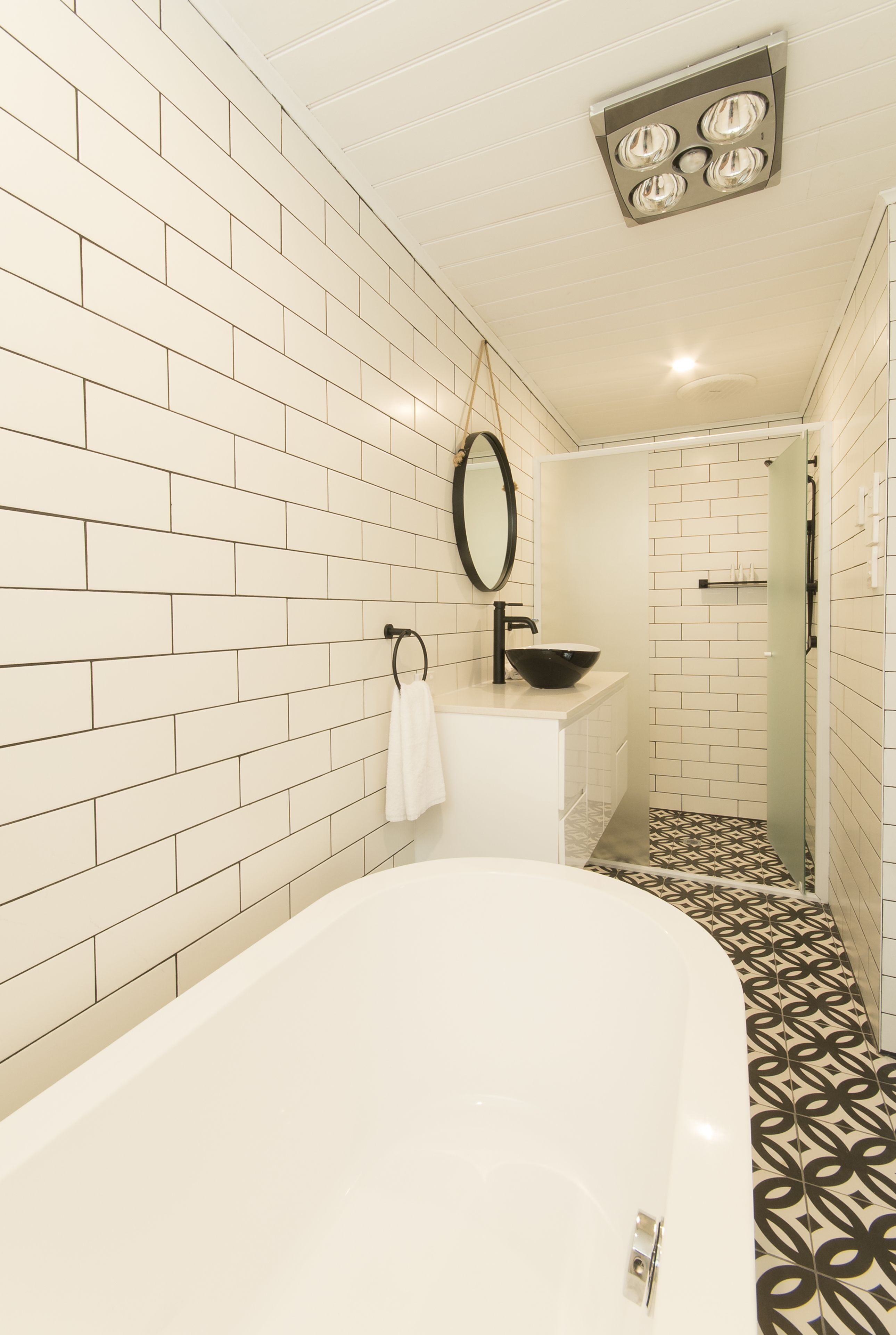 A bathroom with white subway tiles, a white bathtub, a black sink, and a mirror.