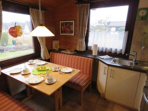 A cozy kitchen with a dining table set for two, a bench, and a window with curtains.