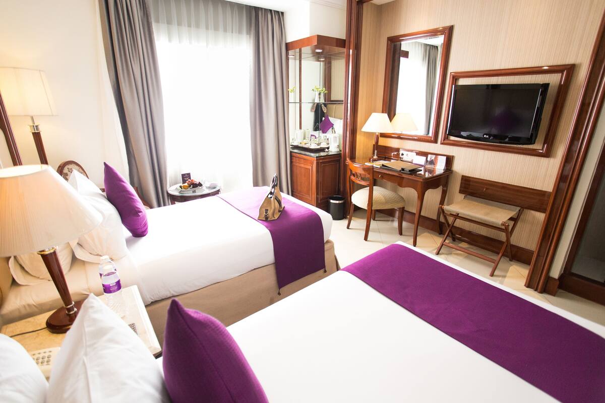 Una habitación de hotel con dos camas, un escritorio, una silla, un televisor y un baño.