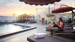 Un área de piscina en la azotea con sillones, una mesa con una bebida y vistas al atardecer.