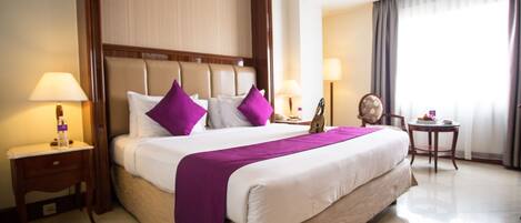 A hotel room with a large bed, two bedside tables, a nightstand, a chair, and a small table with a lamp.