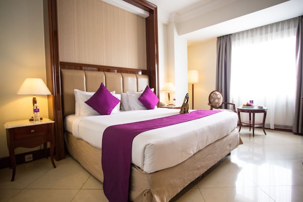Une chambre d’hôtel avec un grand lit, deux tables de chevet, une commode, une chaise et une petite table avec une lampe.