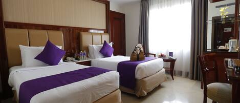 A hotel room with two beds, each with a purple bedspread, a wooden headboard, and a nightstand with a lamp and a phone.