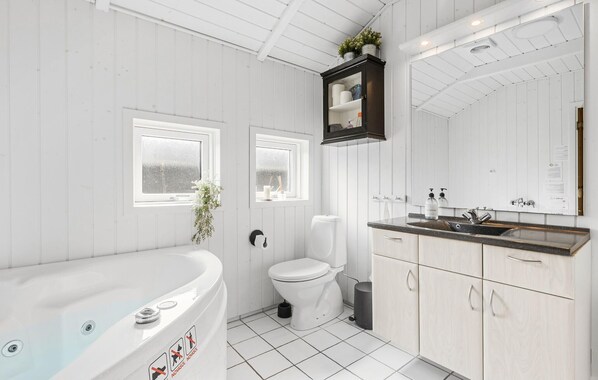 Een moderne badkamer met een wit ligbad, toilet en een wastafel met spiegel erboven.