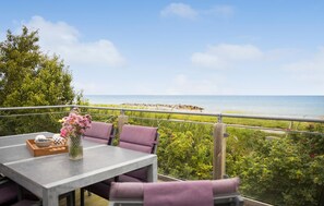 Een balkon met een tafel en stoelen, met uitzicht op een strand en een rotsachtige kustlijn.