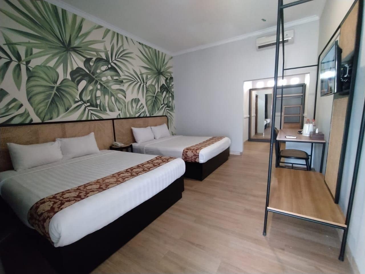 A hotel room with two beds, a desk, and a mirror.