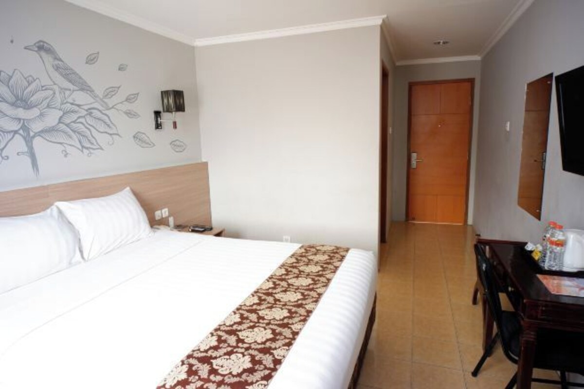 A hotel room with a bed, a wall-mounted TV, a wooden door, and a small table with a chair.