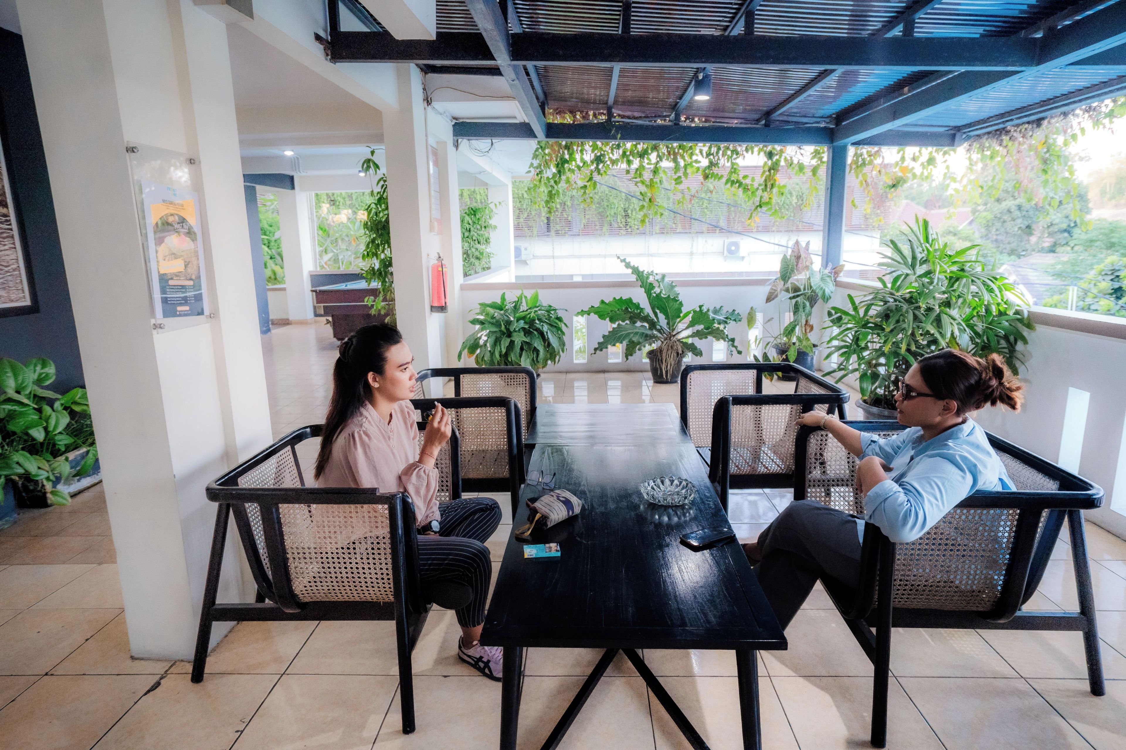 Un área de estar interior con una mesa y sillas, rodeada de plantas en macetas y vistas al verdor exterior.
