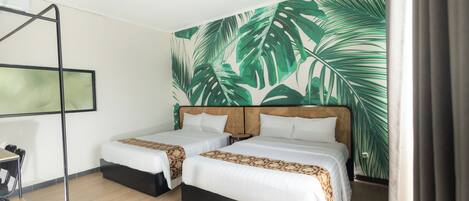 Habitación de hotel con dos camas, piso de madera, pared decorada con hojas tropicales grandes y una silla de metal negro.