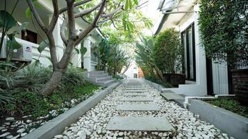 A pathway lined with white pebbles and a tree on the left, leading to a building with a white facade and a staircase.