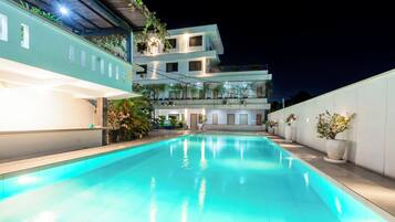 A swimming pool with a clear blue water surface, surrounded by a white wall and a building with multiple balconies.