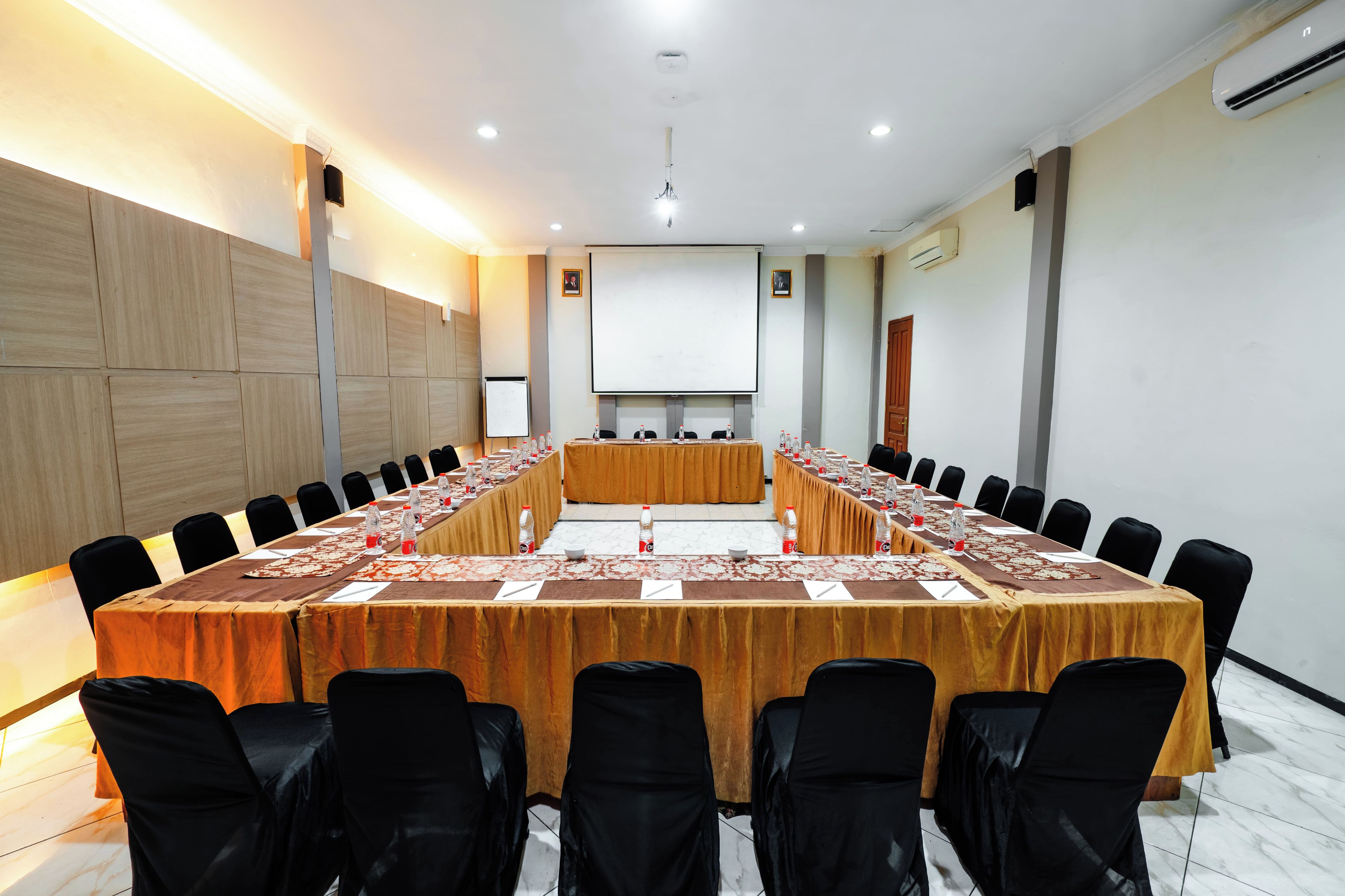 Une salle de conférence avec une longue table, des chaises noires et un écran de projection.