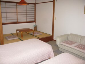 A traditional Japanese room with tatami flooring, a low wooden bench, a futon bed, and a sofa with cushions. - Villa Kubota (Nozawaonsen)