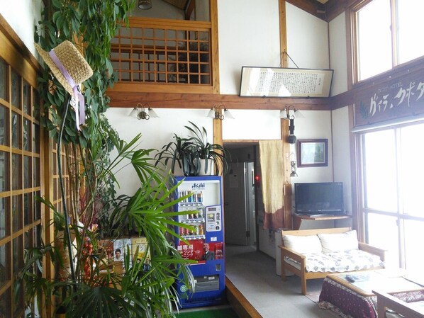 A traditional Japanese room with tatami flooring, a futon bed, a TV, and a vending machine.