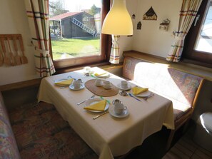 A dining area with a table set for two, a bench, and a window with a view of a building and a ladder outside.