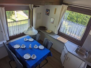 A dining area with a blue table set for four, a hanging lamp, and a view of greenery outside.