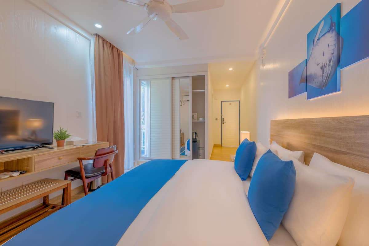 Ein Hotelzimmer mit einem Bett, einem Schreibtisch, einem Sessel, einem Fernseher und einem Deckenventilator.