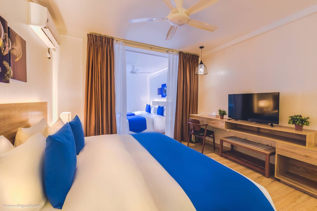 Ein Hotelzimmer mit Bett, Schreibtisch, Fernseher und Deckenventilator.