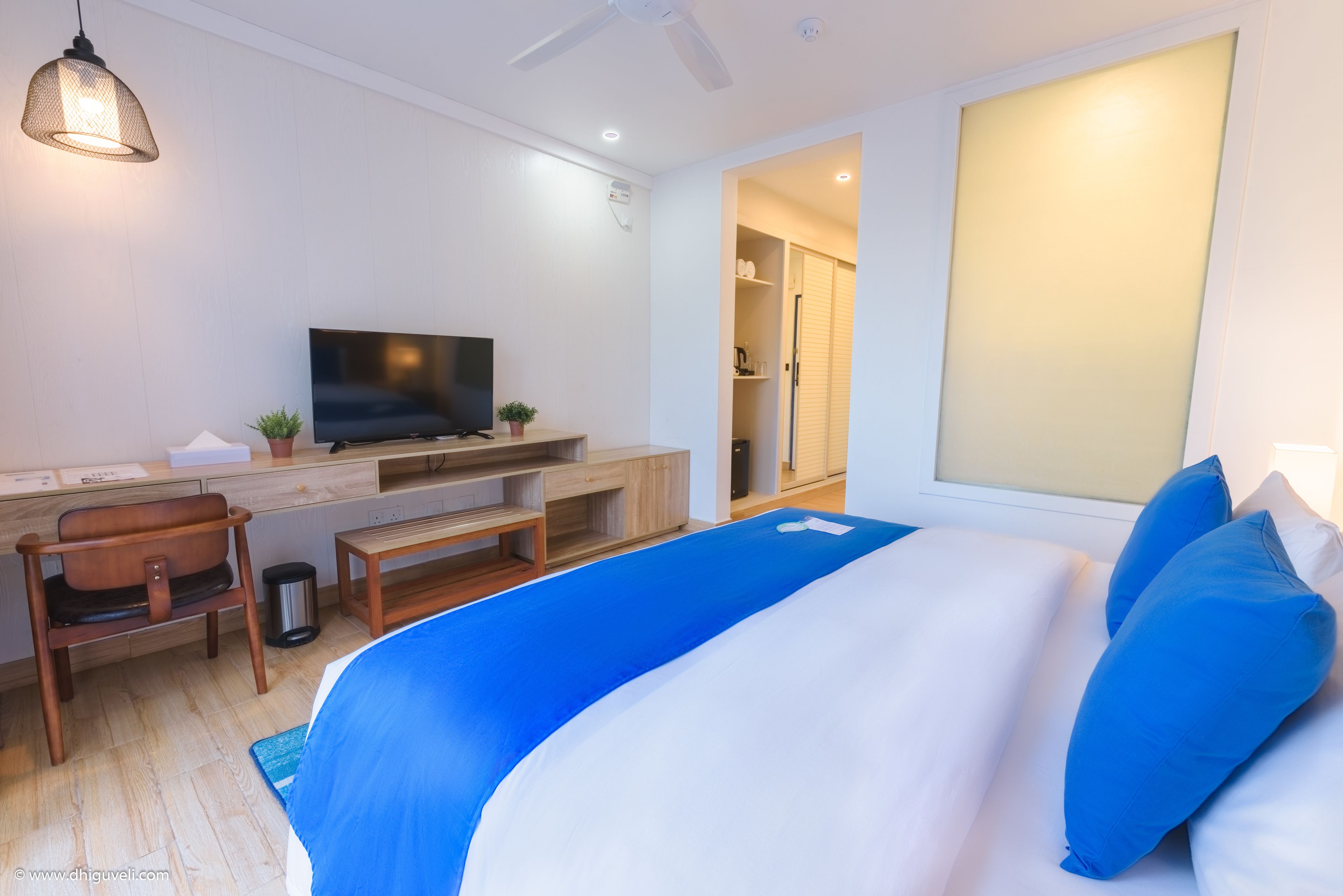 A modern hotel room with a large bed, a desk with a TV, a chair, and a small plant.